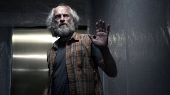 Movie still from “Z Nation” (2014), created by Karl Schaefer – An older man with a beard and a plaid shirt; Medium shot, Low angle