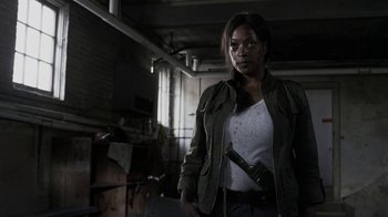 Movie still from “Z Nation” (2014), created by Karl Schaefer – A woman holding a gun in a room; Medium shot, Over the shoulder angle
