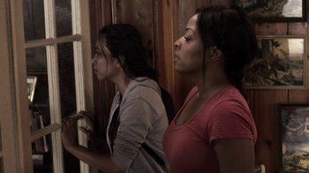 Movie still from “Z Nation” (2014), created by Karl Schaefer – Two young women standing next to each other in front of a window; Medium shot, Over the shoulder angle