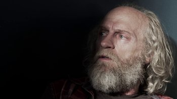 Movie still from “Z Nation” (2014), created by Karl Schaefer – An old man with a beard and a red and white plaid shirt; Close Up shot, Low angle
