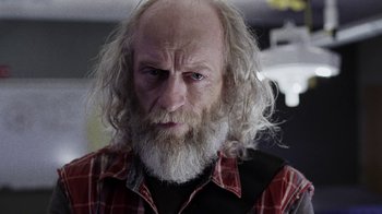 Movie still from “Z Nation” (2014), created by Karl Schaefer – An old man with a long white beard and wearing a plaid shirt; Close Up shot, Low angle
