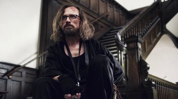 Movie still from “Z Nation” (2014), created by Karl Schaefer – A man sitting on the ground in front of a staircase; Medium shot, Low angle