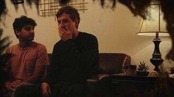 Movie still from “Creep 2” (2017), directed by Patrick Brice – A man sitting on a couch with his hands over his mouth; Medium shot, Over the shoulder angle