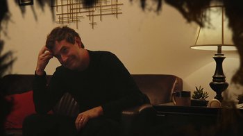 Movie still from “Creep 2” (2017), directed by Patrick Brice – A man sitting on top of a brown leather couch; Close Up shot, Over the shoulder angle