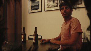 Movie still from “Creep 2” (2017), directed by Patrick Brice – A man sitting at a table with two bottles of beer; Medium shot, Over the shoulder angle