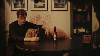 Movie still from “Creep 2” (2017), directed by Patrick Brice – A man sitting at a table with a bottle of beer; Medium shot, High angle