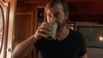 Movie still from “Creep 2” (2017), directed by Patrick Brice – A bearded man drinking a glass of green liquid; Close Up shot, Over the shoulder angle