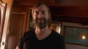 Movie still from “Creep 2” (2017), directed by Patrick Brice – A man with long hair and a goatee is smiling for the camera; Close Up shot, Low angle