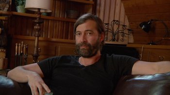 Movie still from “Creep 2” (2017), directed by Patrick Brice – A man sitting on a couch in a living room; Close Up shot, Over the shoulder angle