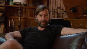 Movie still from “Creep 2” (2017), directed by Patrick Brice – A man sitting on a couch in a living room; Close Up shot, Over the shoulder angle