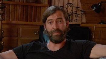 Movie still from “Creep 2” (2017), directed by Patrick Brice – A man with long hair and a beard sitting in a chair; Close Up shot, Over the shoulder angle