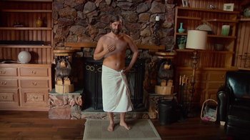 Movie still from “Creep 2” (2017), directed by Patrick Brice – A man standing in front of a fireplace wearing a towel; Wide shot, High angle