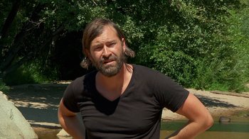 Movie still from “Creep 2” (2017), directed by Patrick Brice – A man with long hair and a black shirt is posing for a picture; Close Up shot, Over the shoulder angle