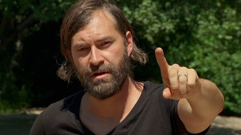Movie still from “Creep 2” (2017), directed by Patrick Brice – A man with long hair and a beard is holding up his middle finger; Close Up shot, Over the shoulder angle