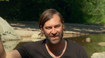 Movie still from “Creep 2” (2017), directed by Patrick Brice – A man with long hair and a goatee is smiling; Close Up shot, Over the shoulder angle
