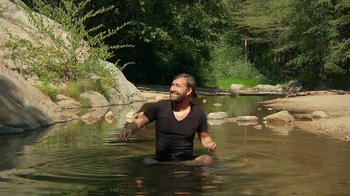 Movie still from “Creep 2” (2017), directed by Patrick Brice – A man sitting in the water in a river; Wide shot, Over the shoulder angle