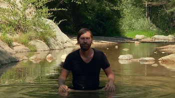 Movie still from “Creep 2” (2017), directed by Patrick Brice – A man sitting in the water of a river; Medium shot, High angle