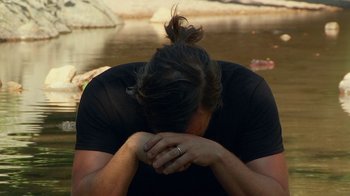 Movie still from “Creep 2” (2017), directed by Patrick Brice – A man with his hands over his face in front of a body of water; Close Up shot, Over the shoulder angle
