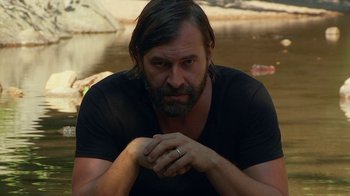 Movie still from “Creep 2” (2017), directed by Patrick Brice – A man with long hair and a beard wearing a black t - shirt; Close Up shot, Over the shoulder angle