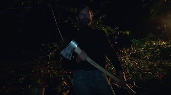 Movie still from “Creep 2” (2017), directed by Patrick Brice – A man holding an axe in the woods at night; Medium shot, Low angle