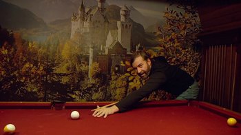 Movie still from “Creep 2” (2017), directed by Patrick Brice – A man leaning over a pool table to hit a white ball; Medium shot, High angle