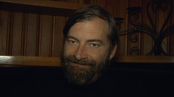 Movie still from “Creep 2” (2017), directed by Patrick Brice – A man with long hair and a goatee is smiling for the camera; Close Up shot, Low angle