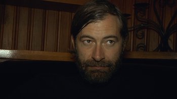 Movie still from “Creep 2” (2017), directed by Patrick Brice – A man with long hair and a goatee is looking at the camera; Close Up shot, Low angle