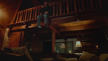 Movie still from “Creep 2” (2017), directed by Patrick Brice – A man sitting on top of a wooden railing holding a laptop; Wide shot, Low angle