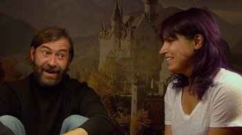 Movie still from “Creep 2” (2017), directed by Patrick Brice – A man and a woman sitting next to each other in front of a castle mural; Medium shot, Low angle