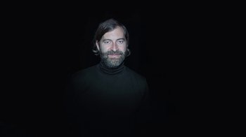 Movie still from “Creep 2” (2017), directed by Patrick Brice – A man wearing a black shirt and a beard; Medium shot, Overhead angle