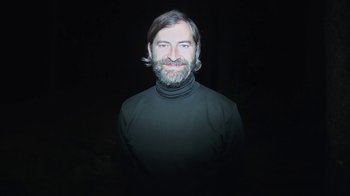 Movie still from “Creep 2” (2017), directed by Patrick Brice – A man in a black shirt with long hair and a beard; Medium shot, High angle