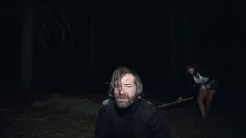 Movie still from “Creep 2” (2017), directed by Patrick Brice – A man in a black shirt with a knife in his mouth; Medium shot, High angle
