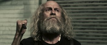 Movie still from “Z Nation” (2014), created by Karl Schaefer – A man with a long beard is looking into the distance; Close Up shot, Low angle