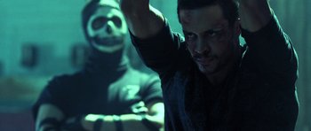 Movie still from “Z Nation” (2014), created by Karl Schaefer – A man in a black shirt is holding a knife in front of a skull; Close Up shot, Over the shoulder angle