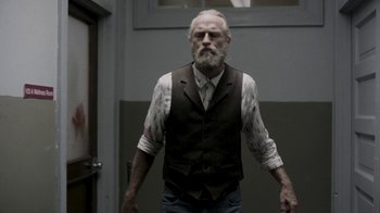 Movie still from “Z Nation” (2014), created by Karl Schaefer – An old man with a beard wearing a vest; Medium shot, Low angle