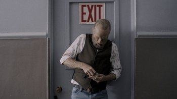 Movie still from “Z Nation” (2014), created by Karl Schaefer – A man standing in front of an exit sign; Medium shot, Over the shoulder angle