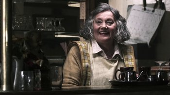 Movie still from “Z Nation” (2014), created by Karl Schaefer – An older woman sitting at a table in a kitchen; Medium shot, Over the shoulder angle