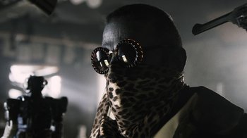Movie still from “Z Nation” (2014), created by Karl Schaefer – A man wearing a leopard print scarf and a pair of round sunglasses; Close Up shot, Low angle