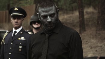 Movie still from “Z Nation” (2014), created by Karl Schaefer – A man in a black dress shirt and tie; Medium shot, Over the shoulder angle