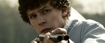 Movie still from “Zombieland” (2009), directed by Ruben Fleischer – A man holding a gun while wearing a blue shirt; Close Up shot, Over the shoulder angle