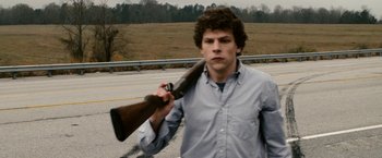 Movie still from “Zombieland” (2009), directed by Ruben Fleischer – A young man holding a rifle in his hand; Medium shot, Over the shoulder angle