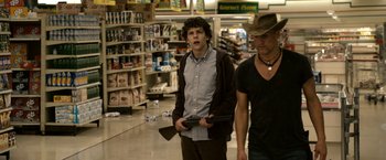 Movie still from “Zombieland” (2009), directed by Ruben Fleischer – Two men walking in a grocery store holding guns; Medium shot, Over the shoulder angle
