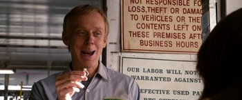 Movie still from “Zombieland” (2009), directed by Ruben Fleischer – A man holding a cigarette in front of a business sign; Close Up shot, Over the shoulder angle