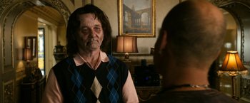 Movie still from “Zombieland” (2009), directed by Ruben Fleischer – An older man in a plaid vest talking to a younger man in front of a painting; Medium shot, Over the shoulder angle