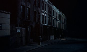 Movie still from “10 Rillington Place” (1971), directed by Richard Fleischer – A dark city street with many buildings lit up at night; Extreme Wide shot, High angle