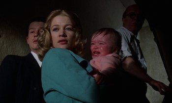 Movie still from “10 Rillington Place” (1971), directed by Richard Fleischer – A woman holding a crying baby in front of other people; Medium shot, Low angle