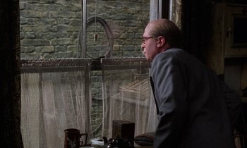Movie still from “10 Rillington Place” (1971), directed by Richard Fleischer – A man in a suit looking out of a window; Medium shot, Over the shoulder angle
