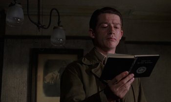 Movie still from “10 Rillington Place” (1971), directed by Richard Fleischer – A man reading a book while standing in front of a lamp; Close Up shot, Low angle
