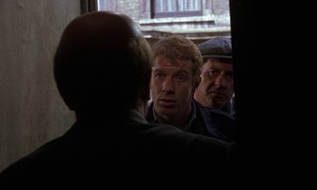 Movie still from “10 Rillington Place” (1971), directed by Richard Fleischer – A group of men standing next to each other in front of a window; Medium shot, Over the shoulder angle