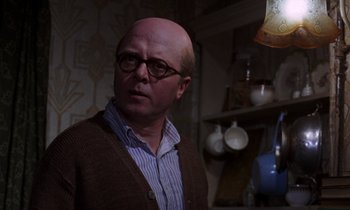 Movie still from “10 Rillington Place” (1971), directed by Richard Fleischer – A bald man wearing glasses and a brown cardigan; Close Up shot, Over the shoulder angle
